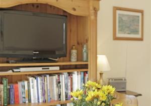 a tv and a book shelf with a television and flowers at The Tack Room in Wangford