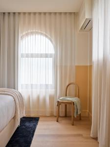 um quarto com uma cama e uma cadeira ao lado de uma janela em The Isla em Batemans Bay