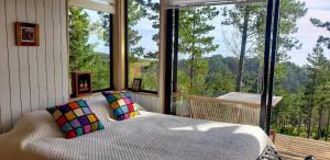een slaapkamer met een bed voor een groot raam bij Tinyhouse Boyeruca Lodge. Maravillosas vistas de Bosque, Mar y Cielo in Vichuquén