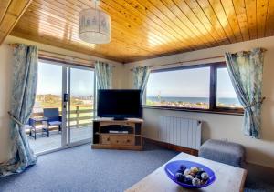 a living room with a television and a balcony with the ocean at Tyn Coed in Moelfre