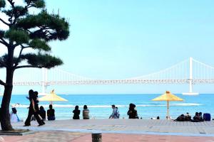 a group of people walking on the beach with a bridge in the background at JJ House Gwangan Beach in Busan