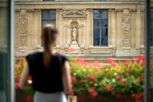 a woman standing in front of a building with flowers at Hôtel Regina Louvre in Paris
