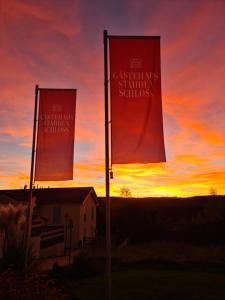 two red flags on a pole with a sunset in the background at Gästehaus Staudenschloss in Mickhausen