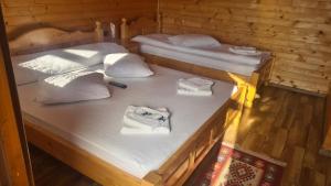 two beds in a wooden cabin with white sheets at Cabanuțele din Lemn in Chişcău