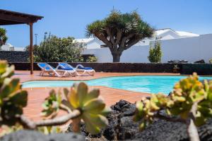 サン・バルトロメにあるCasa Lola Lanzarote piscina climatizada y wifi freeのヤシの木と椅子2脚付きのスイミングプール