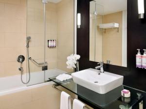 a bathroom with a sink and a shower and a tub at Mövenpick Hotel Jumeirah Lakes Towers Dubai in Dubai
