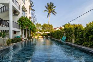 a swimming pool in front of a building with a palm tree at Tra Que Mansion in Hoi An