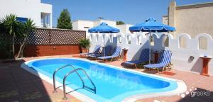 a swimming pool with blue chairs and umbrellas at Pension Stella in Karterados