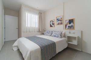 Un dormitorio blanco con una gran cama blanca y una ventana en Las Afortunadas - Playa Arinaga 2ºB, en Arinaga