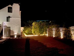 una casa de noche con una pared y árboles en Nature & Sea - Casa Vinhateira East Duplex, en Caloura