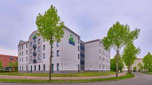 ein weißes Gebäude mit Bäumen vor einer Straße in der Unterkunft Holiday Inn Express Dortmund, an IHG Hotel in Dortmund