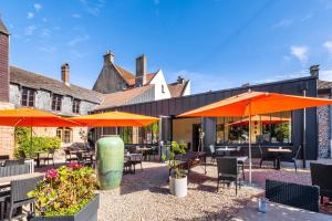 an outdoor patio with tables and chairs and umbrellas at Logis Hôtel & Restaurant - Les Hauts de Montreuil in Montreuil-sur-Mer