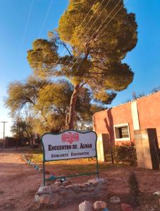 una señal frente a un árbol y un edificio en Encuentro de Almas (Soulmate Encounter) en Tinogasta