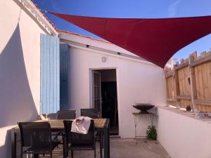 d'une terrasse avec une table et des chaises sous un parasol rouge. dans l'établissement LA CABANE Charmante petite maison 2 chambres à 2,5km plage, à Saint-Georges-dʼOléron