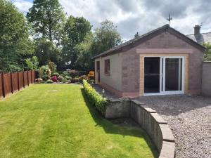 un jardín con una pequeña casa con un patio de césped en Glencoe House Inverness, en Inverness