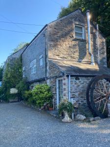 a stone house with a large wheel in front of it at The Granary at Bissick Old Mill in Truro