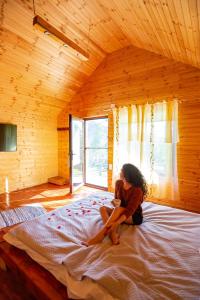 a woman sitting on a bed in a wooden room at Complex turistic Traisteni din Valea Doftanei in Podu lui Neag