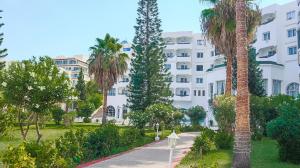 a large white building with palm trees and a sidewalk at Hotel Royal Jinene Sousse in Sousse