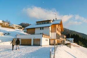 two people walking in the snow in front of a building at Hotel Dreiländerblick Dornbirn in Dornbirn