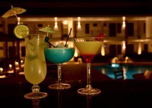 three cocktails sitting on a bar with a pool at Hotel Agualcas in Managua