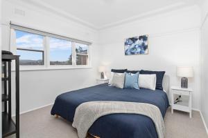 a white bedroom with a blue bed and a window at The Little Lake House in Primbee