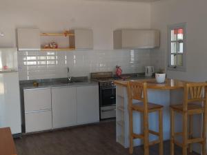 uma cozinha com armários brancos e um balcão com cadeiras em Cabaña Los Pajaritos em Villa Rumipal