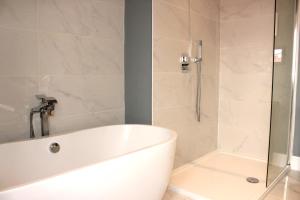 a white bath tub in a bathroom with a shower at Lovely, cosy 3 bedroom apartment in Teddington