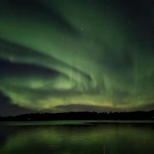 una aurora boreal sobre un cuerpo de agua por la noche en Revontulen Tupa en Kaamanen