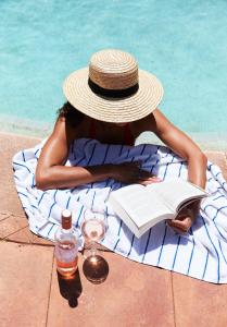 a woman sitting on a towel with a book and a hat at The Continental Hotel in Broome