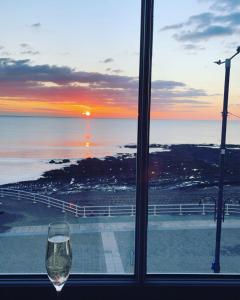 a wine glass sitting in front of a window with the sunset at Sea View Apartment - Sleeps 2 in Aberystwyth