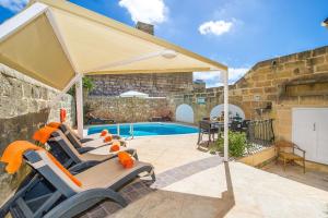eine Terrasse mit Stühlen und einem Sonnenschirm neben einem Pool in der Unterkunft Gawhra Holiday Home in Xagħra