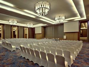 una gran sala de conferencias con sillas blancas y lámparas de araña en Mercure Serpong Alam Sutera, en Serpong