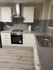 a kitchen with white cabinets and a stove and a sink at Dorcas Lodge - Lovely 5 Bedroom home with free parking and Wi-Fi in Nevendon