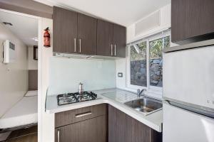 uma cozinha com armários de madeira, um lavatório e uma janela em Mobile Home Next 229 em Pietra Ligure