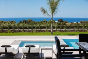 a patio with chairs and a pool with the ocean in the background at Alma Villa, 2000m2 Luxury Living, by ThinkVilla in Angeliana