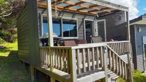 a green tiny house with a deck with a grill at Marina Vista Cabin in Tutukaka