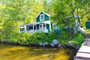a green house sitting on the side of a river at Cottage on Geneva Point in Moultonborough