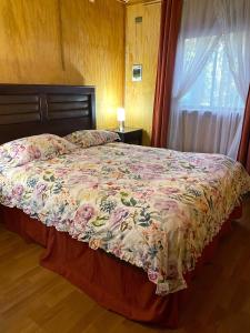 1 dormitorio con 1 cama con colcha de flores y ventana en Cascadas del Llaima, Cabaña Pájaro Carpintero, en Curacautín