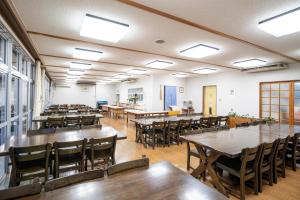 Habitación grande con mesas, sillas y ventanas. en iseshima youth hostel en Shima