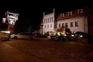 een straat met auto's die 's nachts voor gebouwen geparkeerd staan bij Hotel Zameczek in Książ Wielki