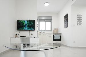 a white kitchen with a glass table and a tv at Sea and Soul in Eilat