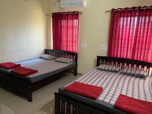 two beds in a room with red curtains at Adheesh Lodge in Dharmastala