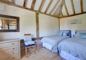 a bedroom with two beds and a dresser and a chair at Barley Byre in Rolvenden