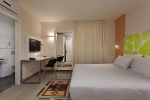 Habitación de hotel con cama, escritorio y TV. en Desert Iris Hotel en Yeroẖam