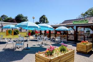 une terrasse avec des chaises et des parasols bleus en face d'un magasin dans l'établissement Team Holiday - Camping de l'Etang du Pays Blanc, à Guérande