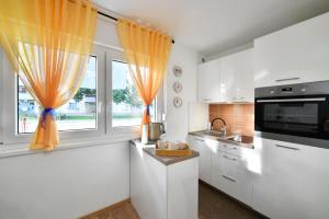 a kitchen with white cabinets and windows with orange curtains at Studio Apartment Aneta in Zagreb +5 photos