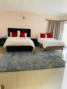 1 dormitorio con 2 camas con almohadas rojas y alfombra en Styled bed and breakfast, en Palapye