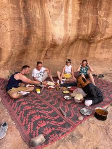 grupa ludzi siedzących na kocu z jedzeniem w obiekcie Wadi Rum Quiet Sky w mieście Wadi Rum