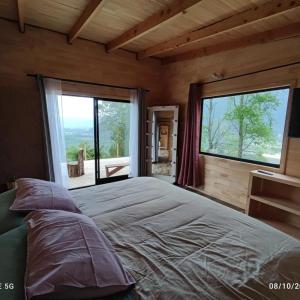 a bedroom with a large bed and large windows at cabaña vista nilahue in Ranco