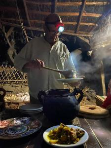 a man stirring a pot on a table with plates of food at Le Sommet Naturel in Chefchaouene